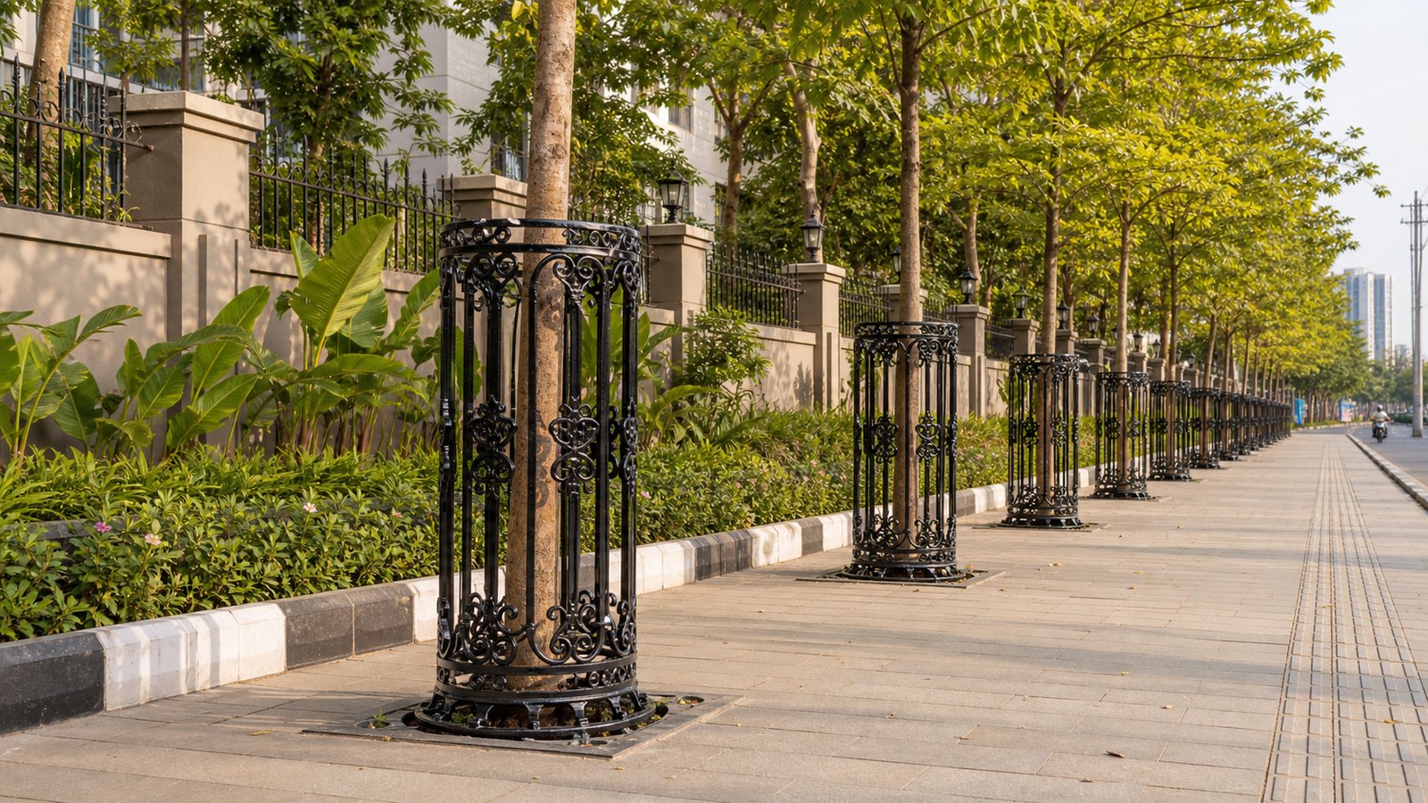 Decorative black cast iron tree guards installed along an Indian urban avenue footpath